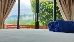 Ein Hotelzimmer mit einem Bett, beigen Vorhängen und Blick auf Grün und Berge durch ein großes Fenster.