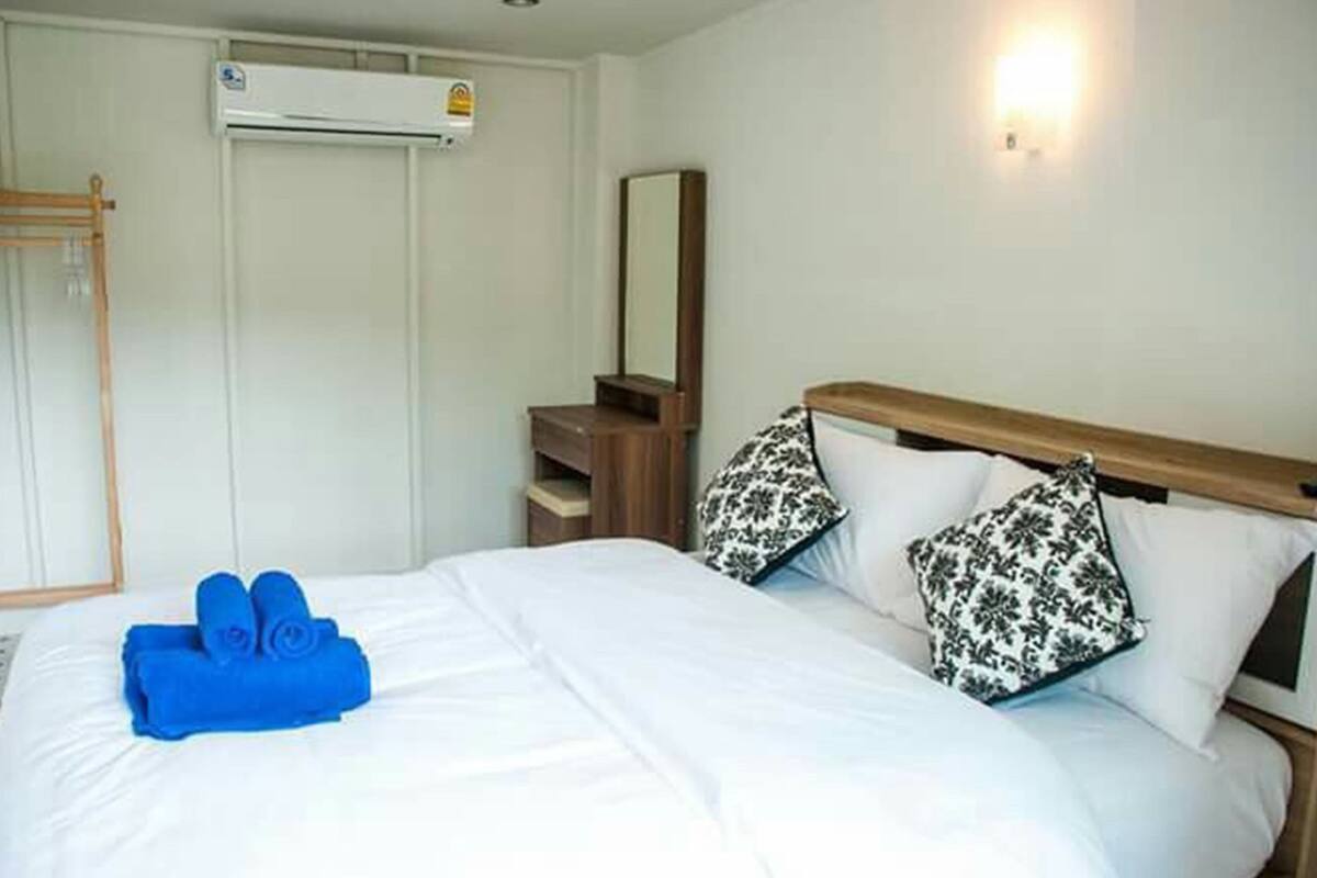 A hotel room with a bed, a bedside table, a mirror, and an air conditioning unit.