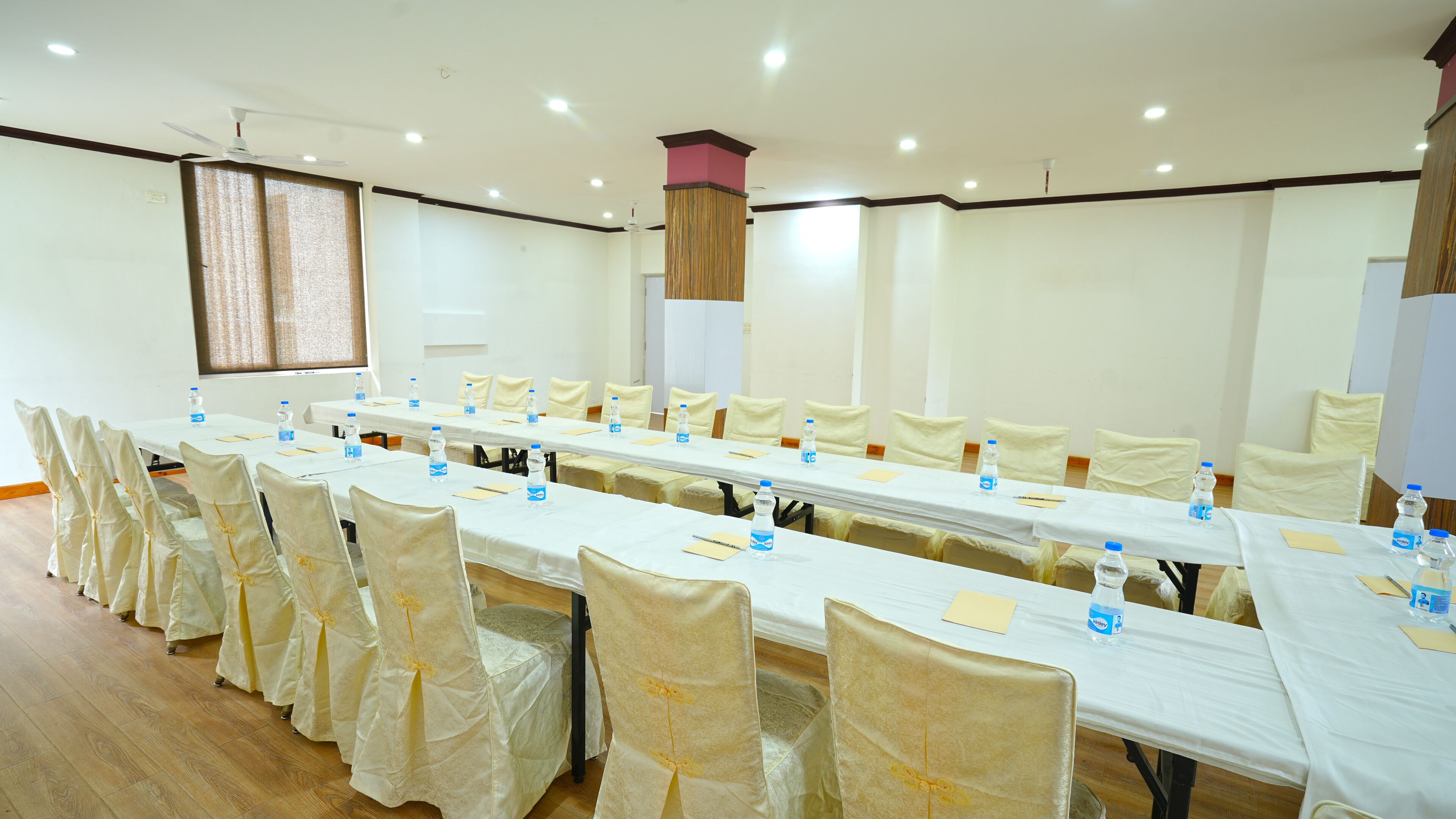 A conference room with a long table, chairs, water bottles, and a ceiling fan.