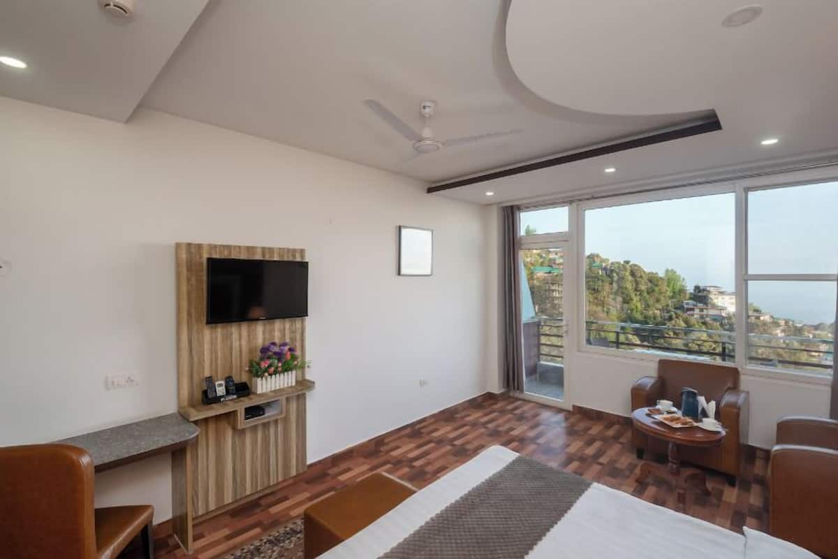 Una habitación de hotel moderna con un mueble bajo de televisión de madera, un televisor de pantalla plana, una zona de comedor con mesa y sillas, y un amplio ventanal con vistas panorámicas.