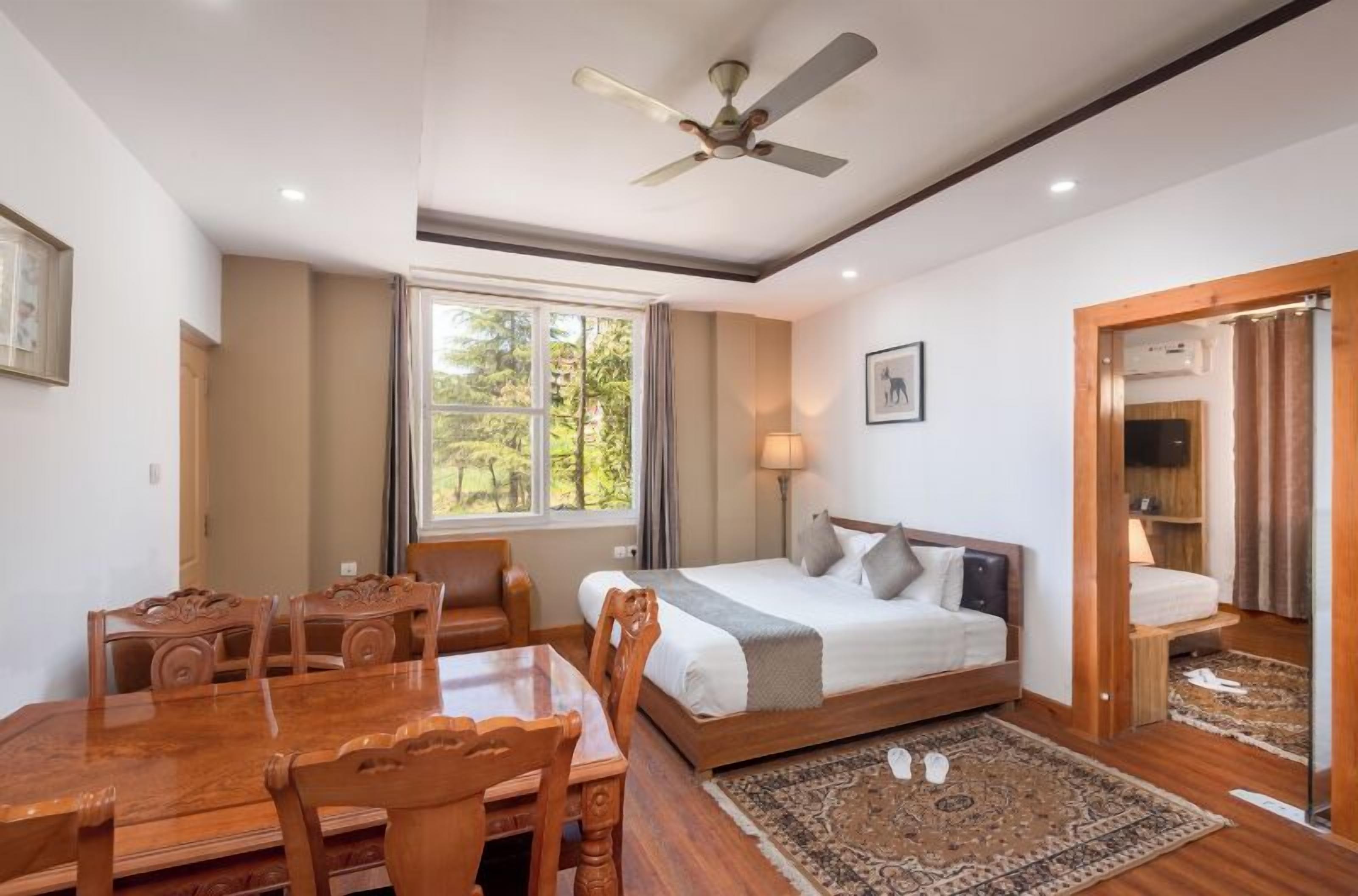 A bedroom with a bed, a desk, chairs, a ceiling fan, a window, and a door.
