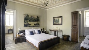 A bedroom with a large bed, a nightstand, a dresser, a painting on the wall, and a door.