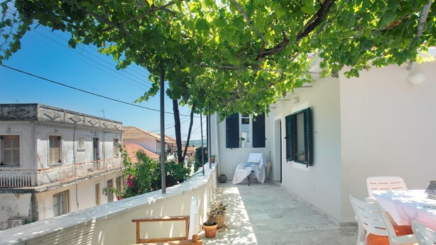 A balcony with a table and chairs, potted plants, and a view of neighboring buildings.