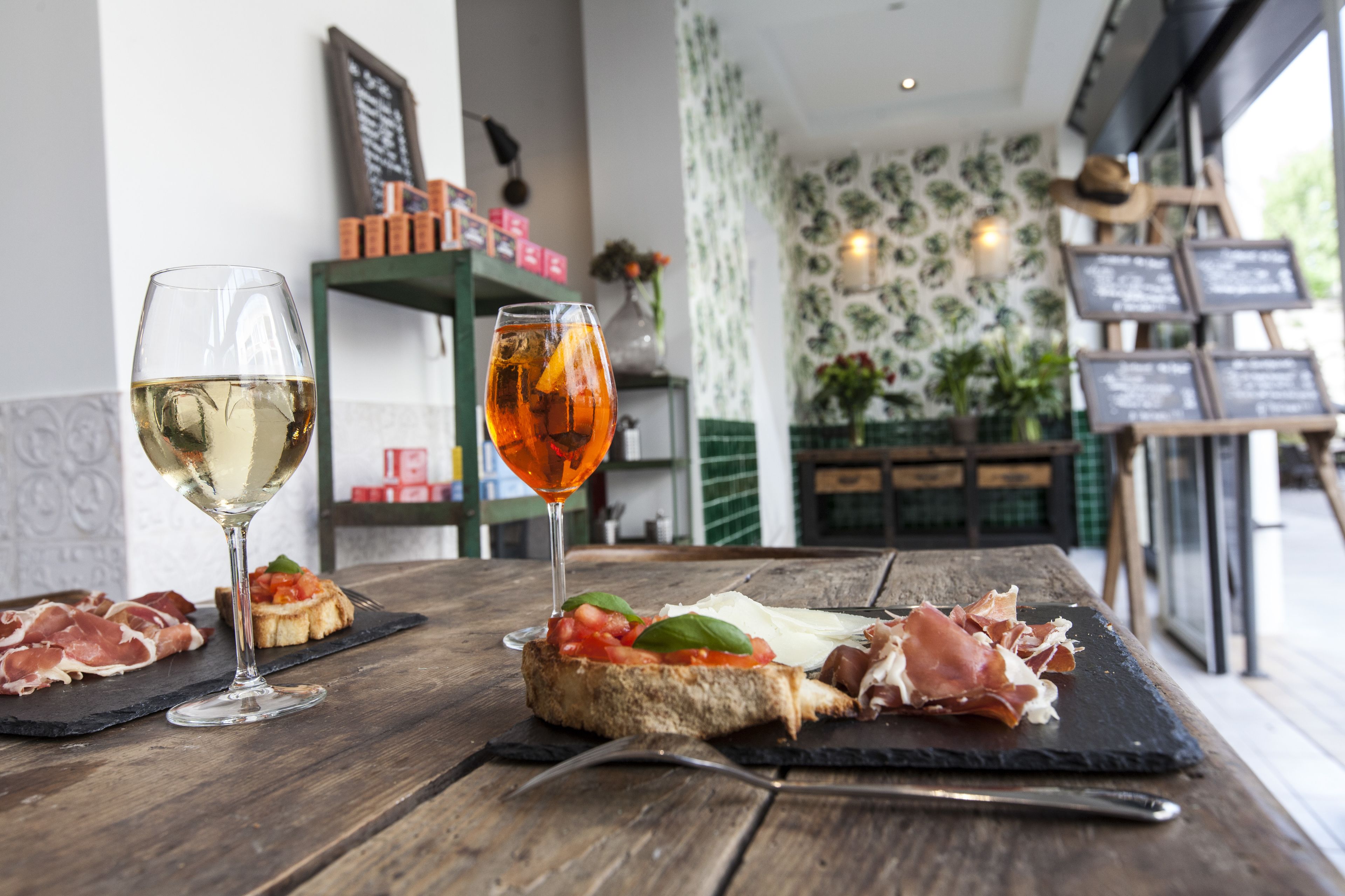 A wooden table with a glass of white wine, a glass of red wine, and a plate of bruschetta with prosciutto and tomatoes.
