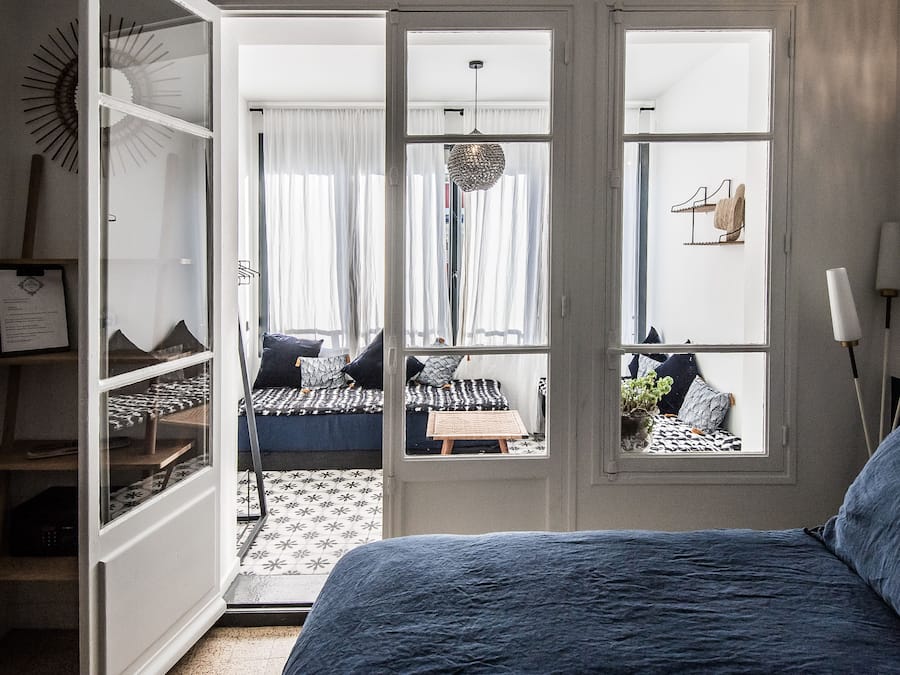 Un dormitori amb un llit gran, un armari i vista a una habitació contigua a través d'una porta de vidre.