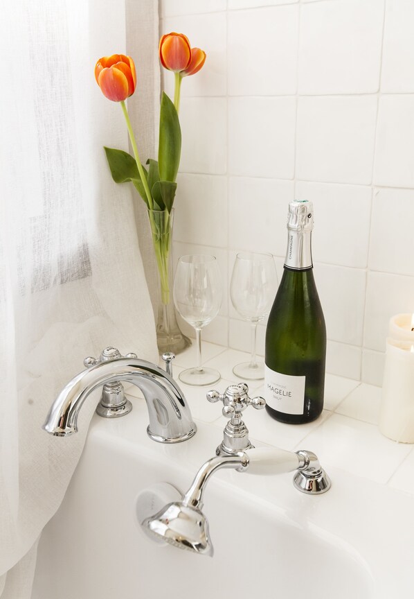 Un baño con un lavamanos blanco, dos tulipanes, una botella de vino espumoso Magelie Brut y dos copas de vino vacías.