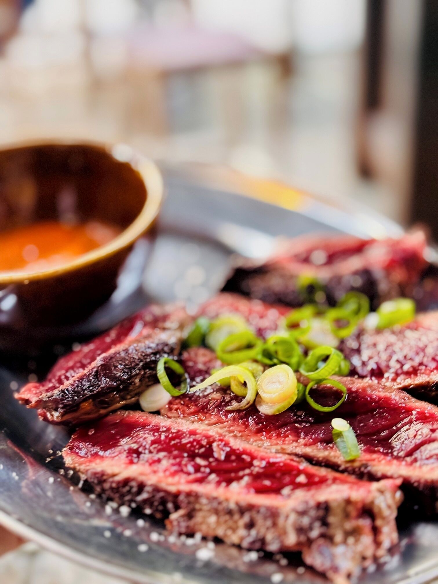 A plate of sliced meat with green onions and a small bowl of sauce.