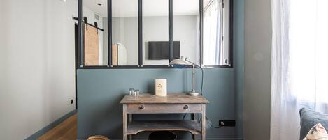 A room with a wooden desk, a chair, a wall-mounted TV, and a window with curtains.