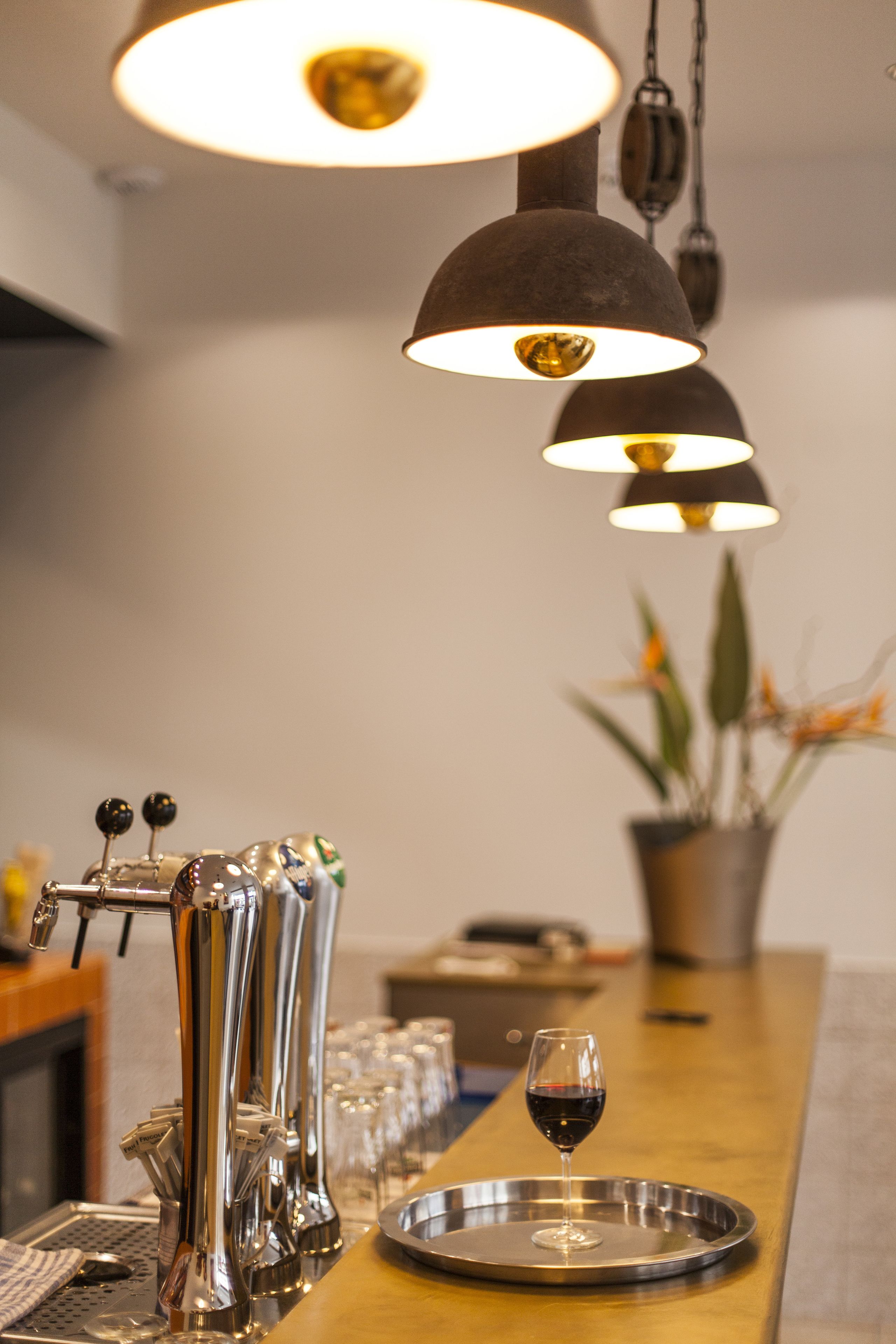 Un coin bar avec un verre à vin posé sur un plateau, un robinet et une plante en pot en arrière-plan.