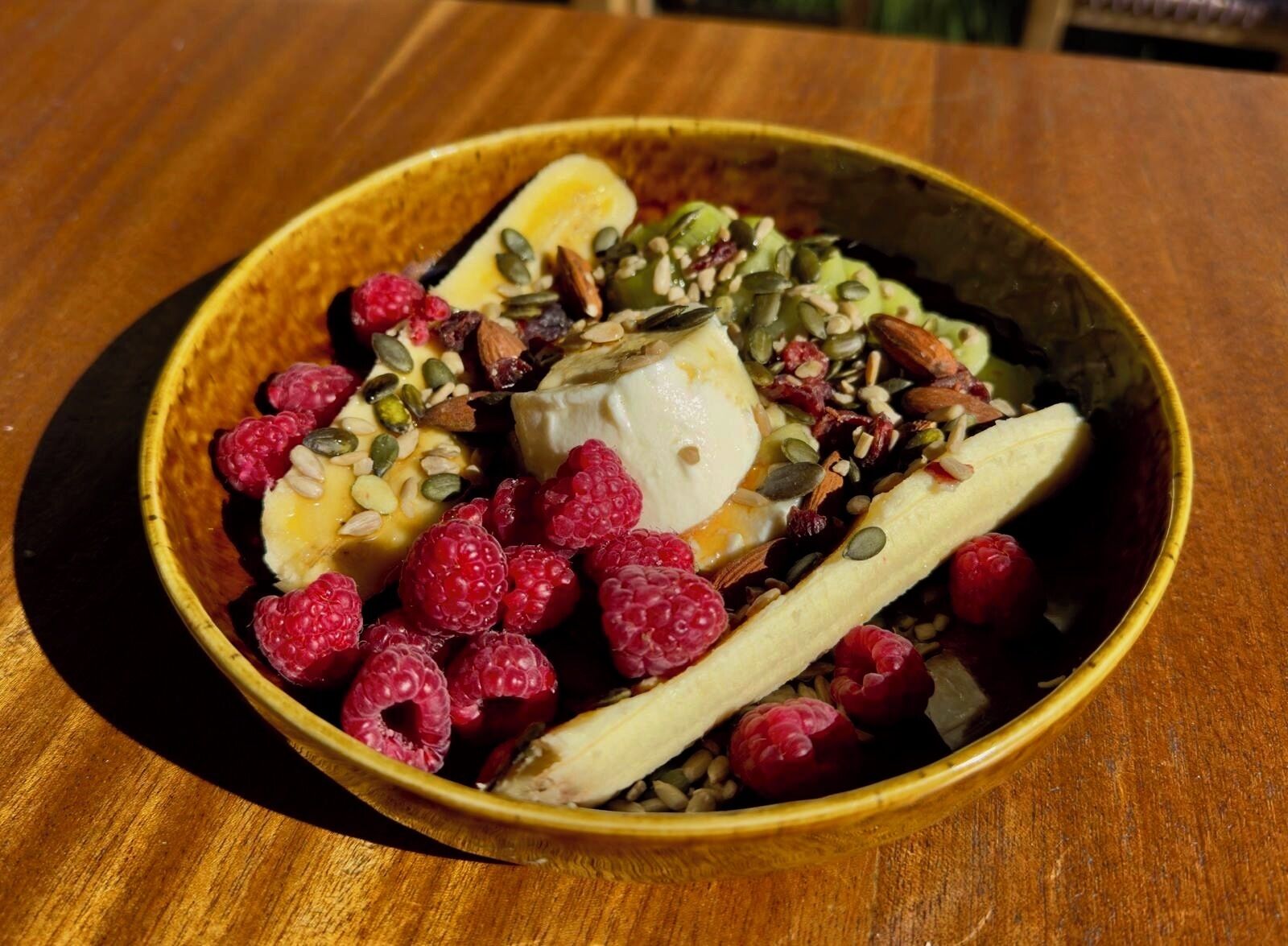 A bowl of food with a banana, raspberries, and nuts.