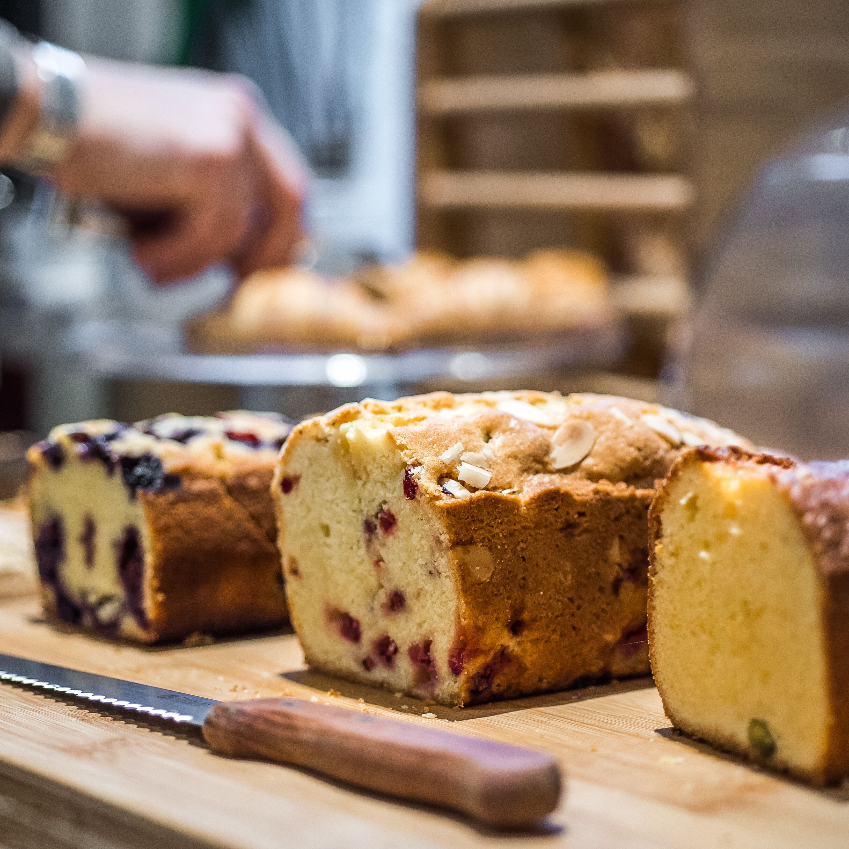 A loaf of fruitcake with visible fruit pieces and nuts, placed on a wooden cutting board with a knife beside it.