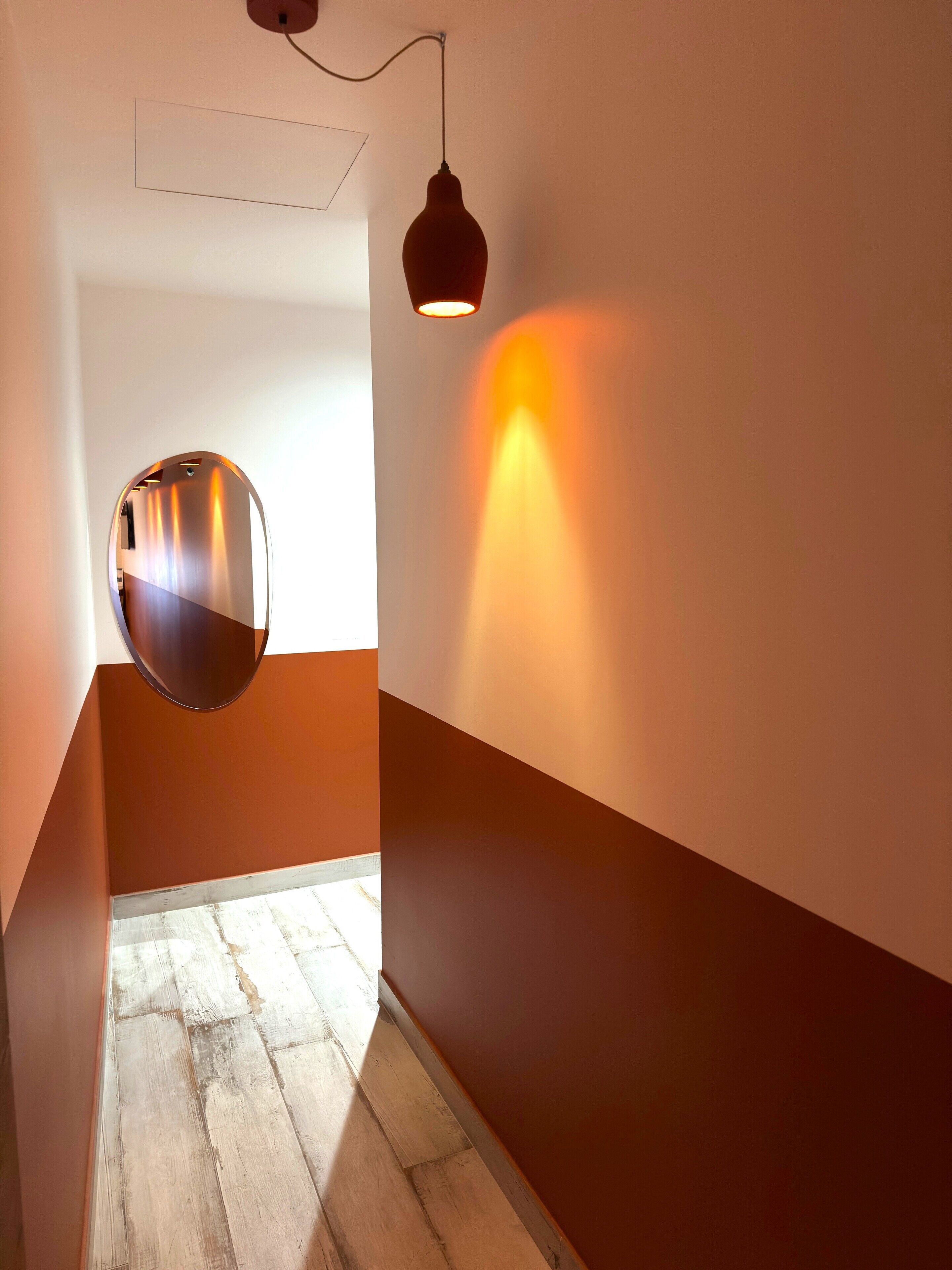 A hallway with a wooden floor, a round mirror, and a wall-mounted light fixture.