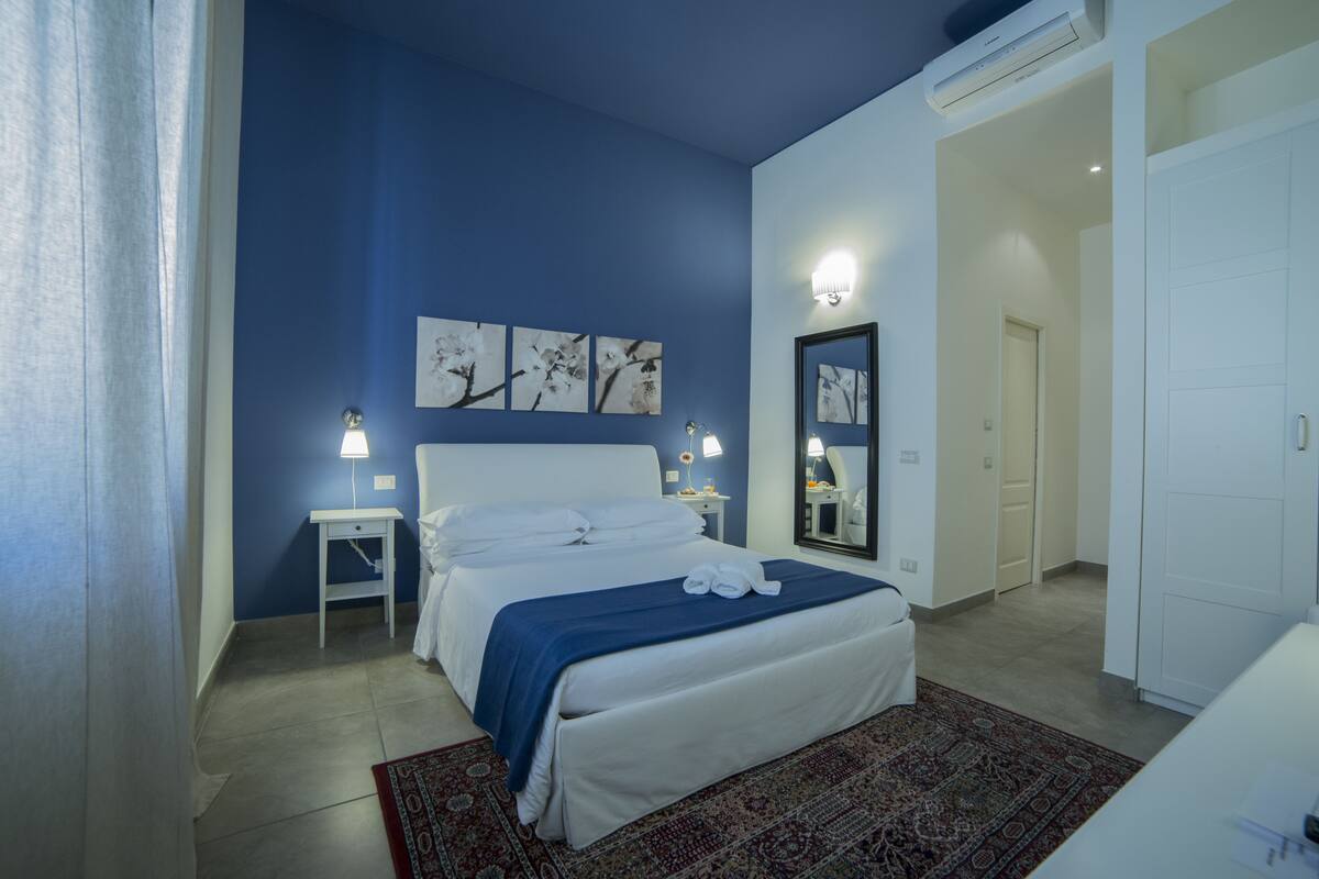 A bedroom with a bed, a nightstand, a wall-mounted lamp, and a mirror.