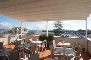 A terrace with outdoor seating, a view of the marina, and a cityscape in the background. - B&B Suite Paciotti (Trani)