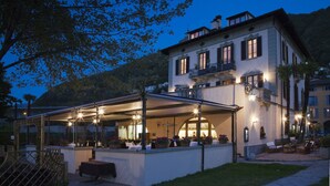A restaurant with outdoor seating, a covered patio, and a mountain backdrop.