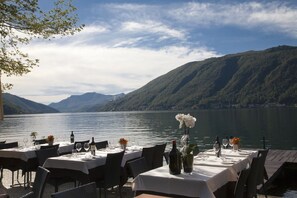 A lakeside restaurant with tables set for dining, overlooking a lake and mountains. - Albergo Ristorante La Palma (Bissone)