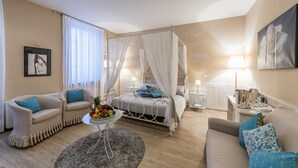 A bedroom with a four-poster bed, two armchairs, a coffee table with fruit, and a bedside table with a lamp.