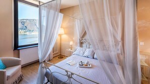 A bedroom with a four-poster bed, a bedside table with a lamp, and a view of a lake and hills.