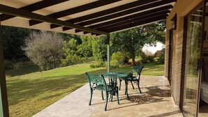 Une terrasse extérieure avec une table et des chaises, une pergola au-dessus et une vue sur un jardin aménagé.