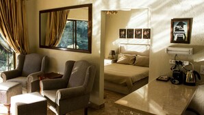 Une chambre avec un lit, deux fauteuils, une table de chevet avec une lampe, un téléviseur et une fenêtre avec des rideaux.
