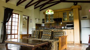 Un coin repas avec une table en bois et des coussins à motifs, une cuisine avec des meubles en bois et un four à micro-ondes, et un plafond avec des poutres apparentes.