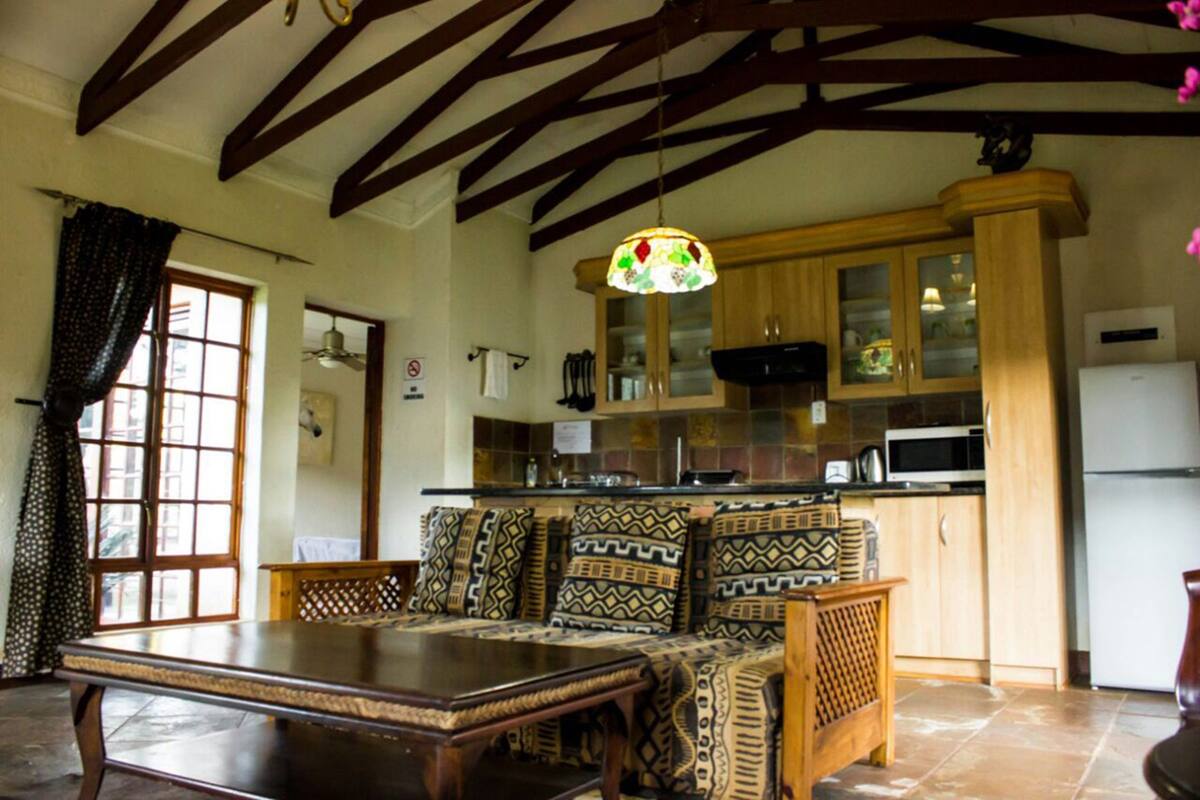 A dining area with a wooden table and patterned cushions, a kitchen with wooden cabinets and a microwave, and a ceiling with exposed beams.