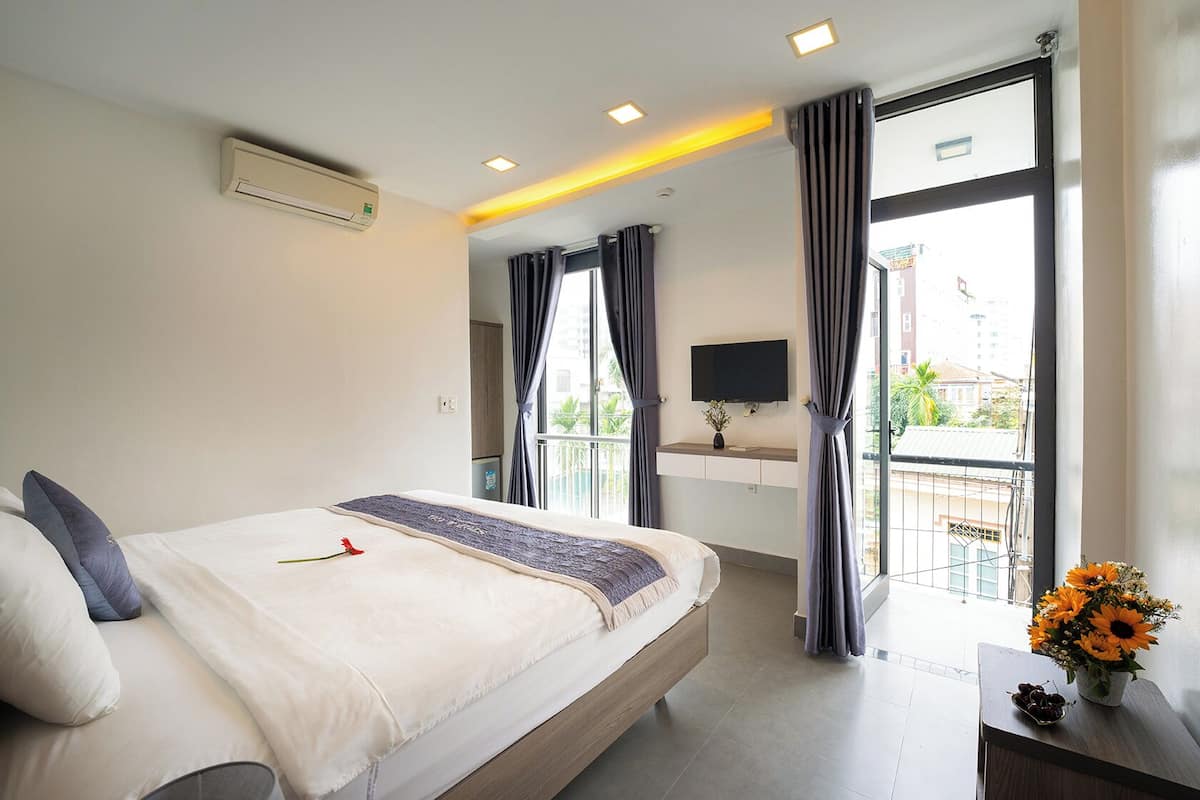 A hotel room with a bed, a TV, a balcony with curtains, and a view of the outside.