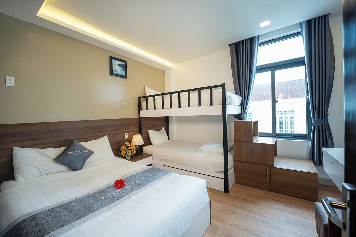 A hotel room with a bunk bed, a desk, a chair, a lamp, and a window with curtains.