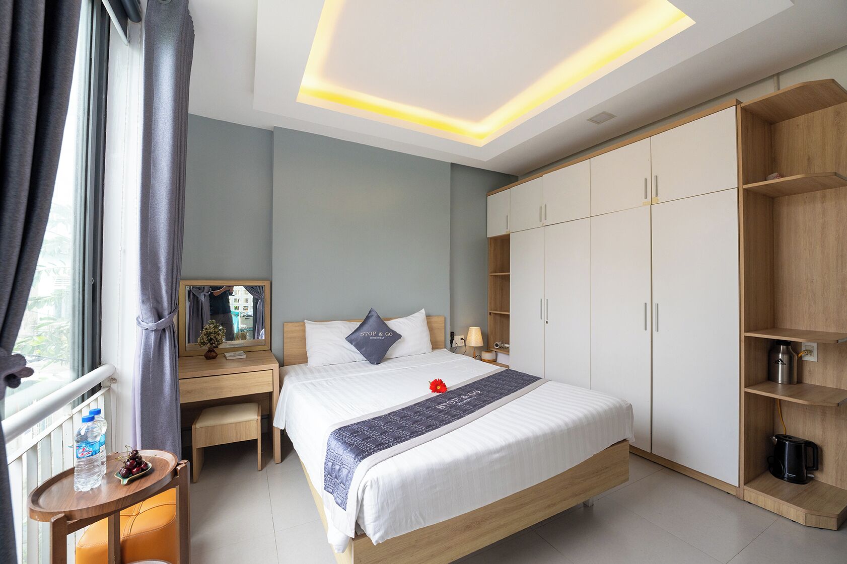 A modern hotel room with a large bed, a desk, a wardrobe, and a window with curtains.