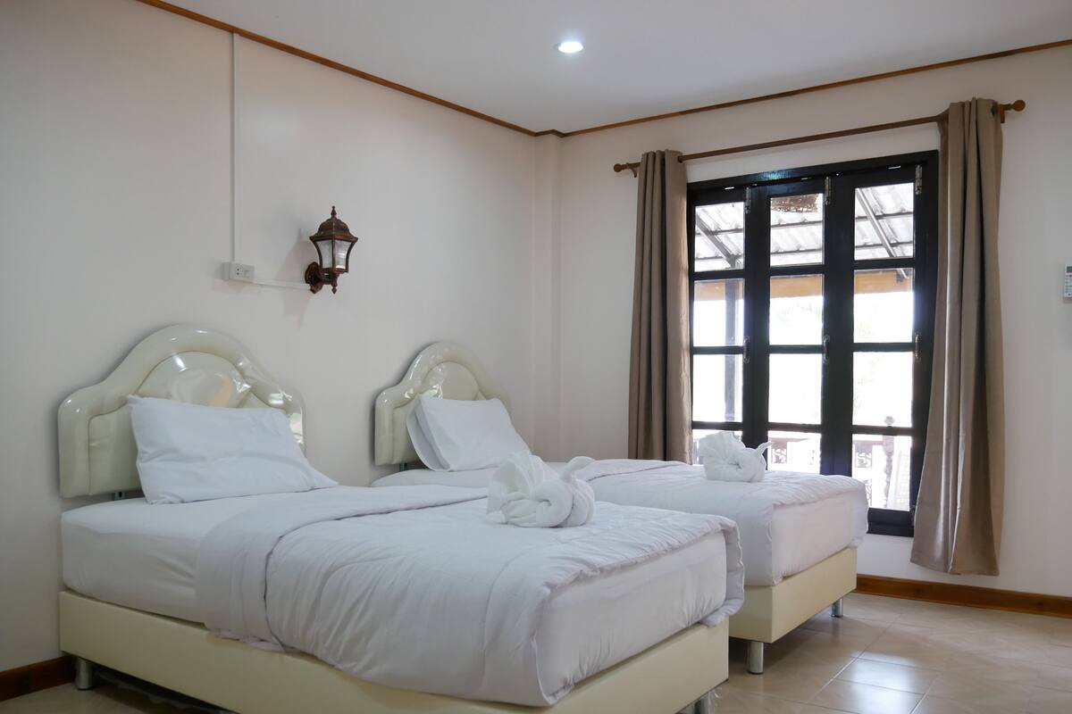 Habitación de hotel con dos camas, una lámpara fijada a la pared y un ventanal con cortinas.