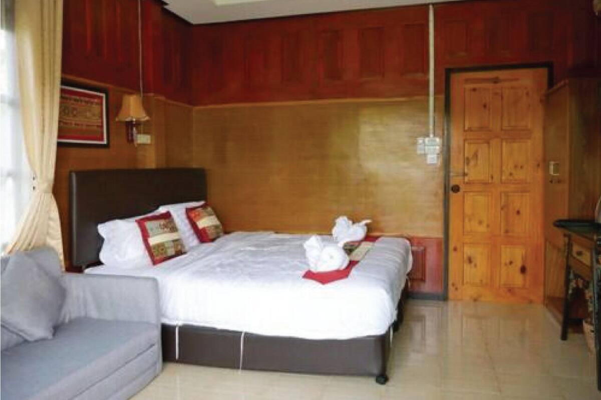Habitación de hotel con una cama grande, un sofá gris, paneles de madera y una puerta de madera.