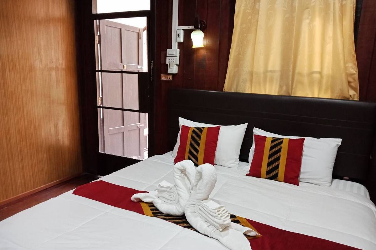 Una habitación de hotel con una cama, un cojín a rayas rojo y blanco, una toalla blanca y una puerta de madera.