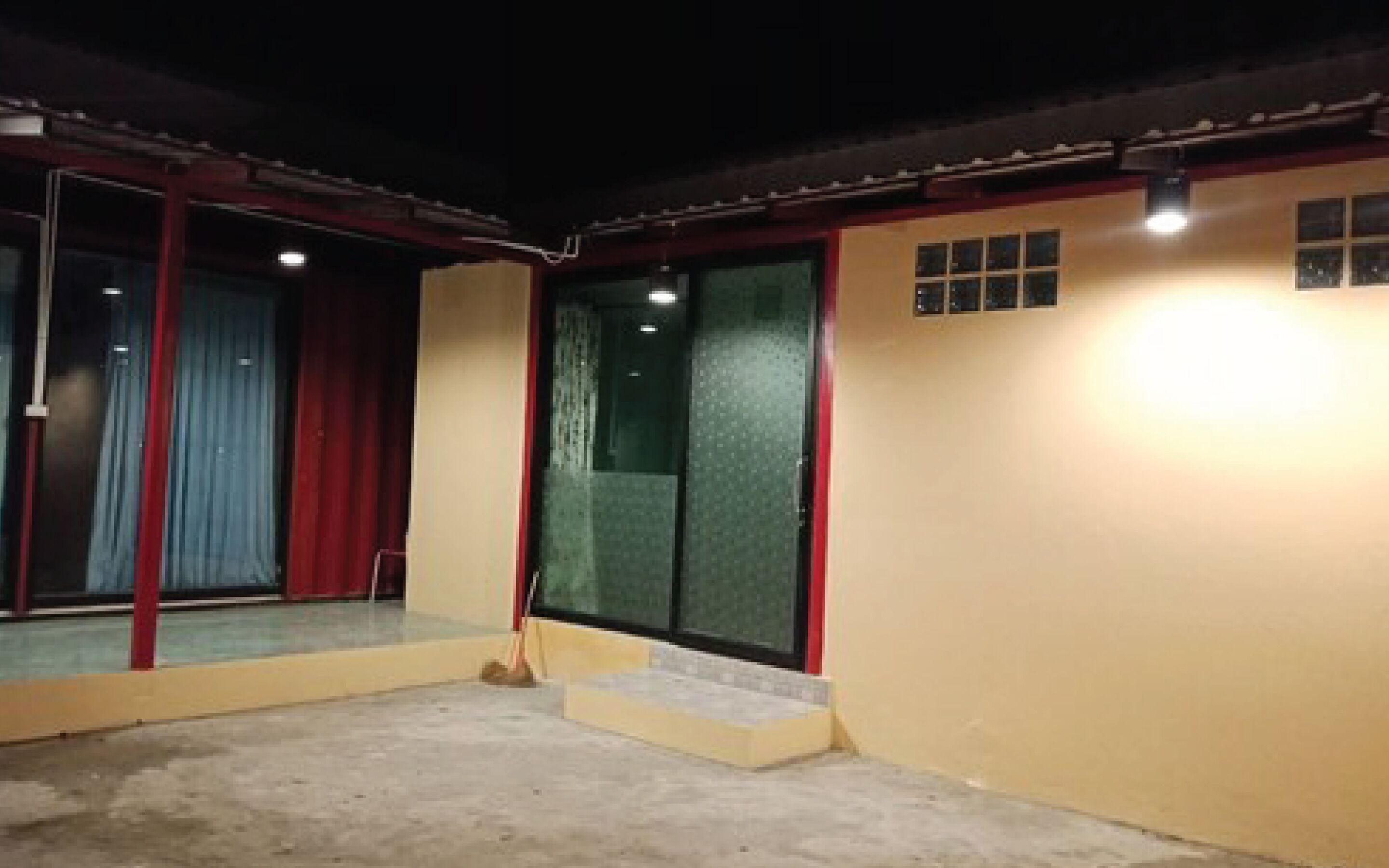 Un edificio con fachada amarilla, una puerta roja y un acceso de vidrio a un área cubierta.
