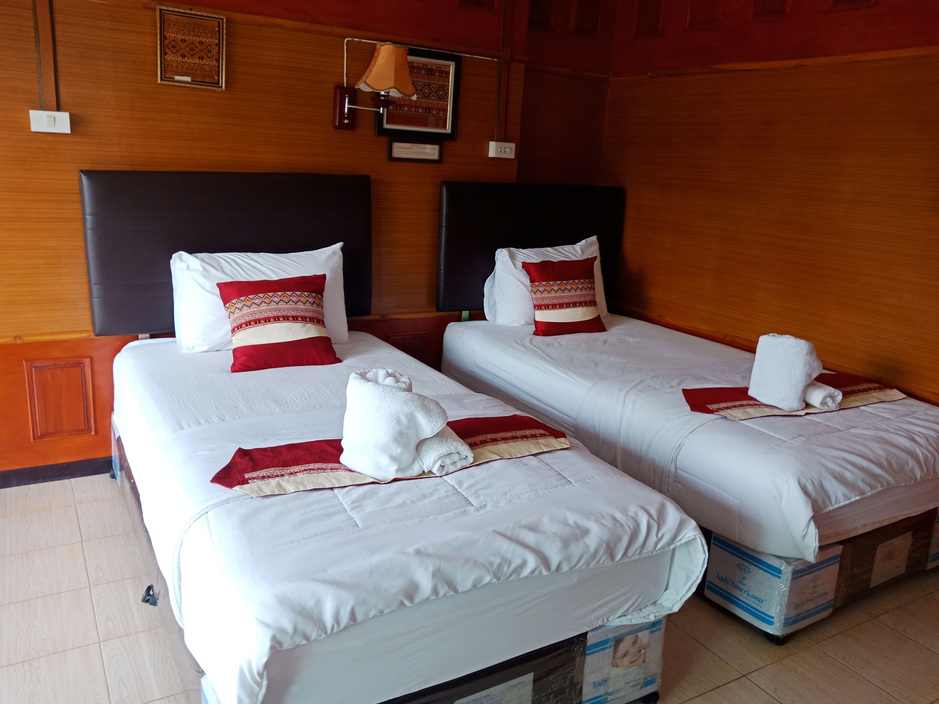 Deux lits simples avec du linge de lit blanc et des touches de rouge, une tête de lit en bois et une lampe fixée au mur.
