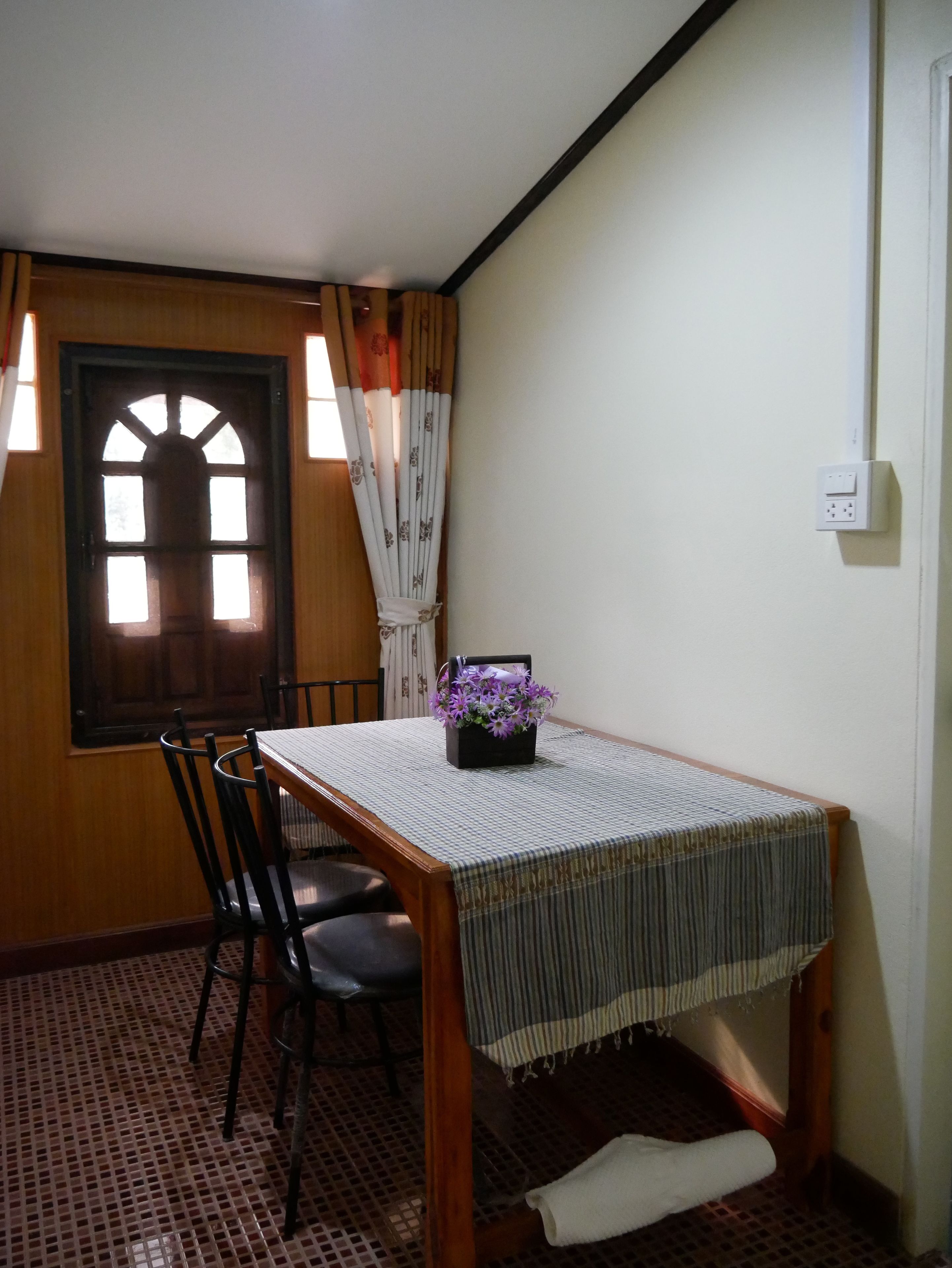 Zona pranzo con tavolo in legno, sedie, finestra con tende e pavimento piastrellato.