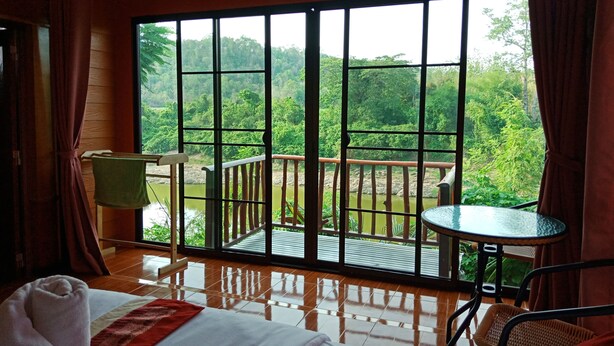 Habitación de hotel con un amplio ventanal corredero que da a un balcón con vistas a un área boscosa.