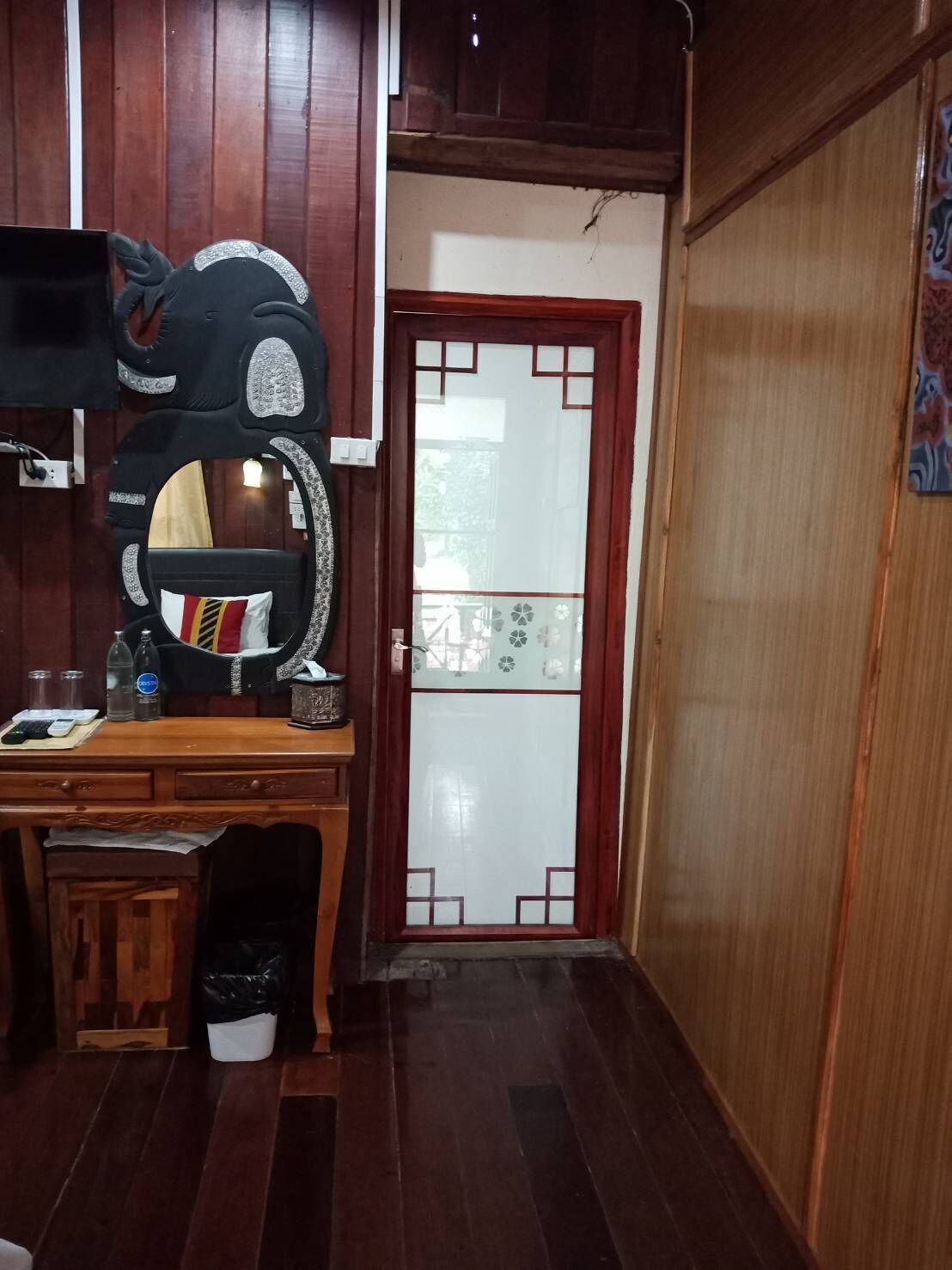 A room with a wooden desk, a chair, a mirror, and a door with decorative glass panels.