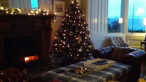 A cozy living room with a fireplace, a Christmas tree, and a large window with curtains. - Cragowlet House East (Helensburgh)