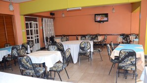 A dining area with multiple tables and chairs, a television mounted on the wall, and a window with curtains. - Hotel Southern Blue (Nairobi)