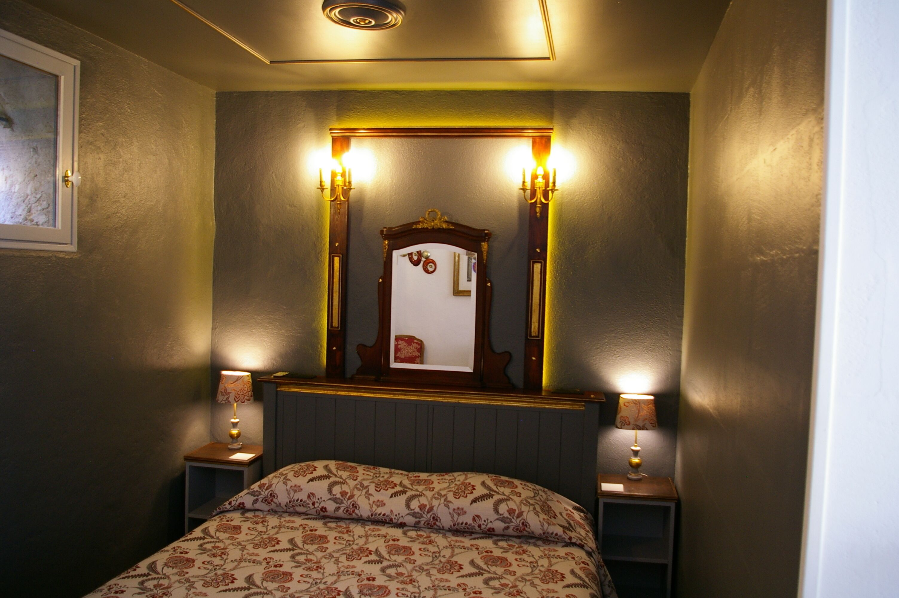 Una camera da letto con un letto, due comodini con lampade, uno specchio con luci a parete e un quadro appeso al muro.