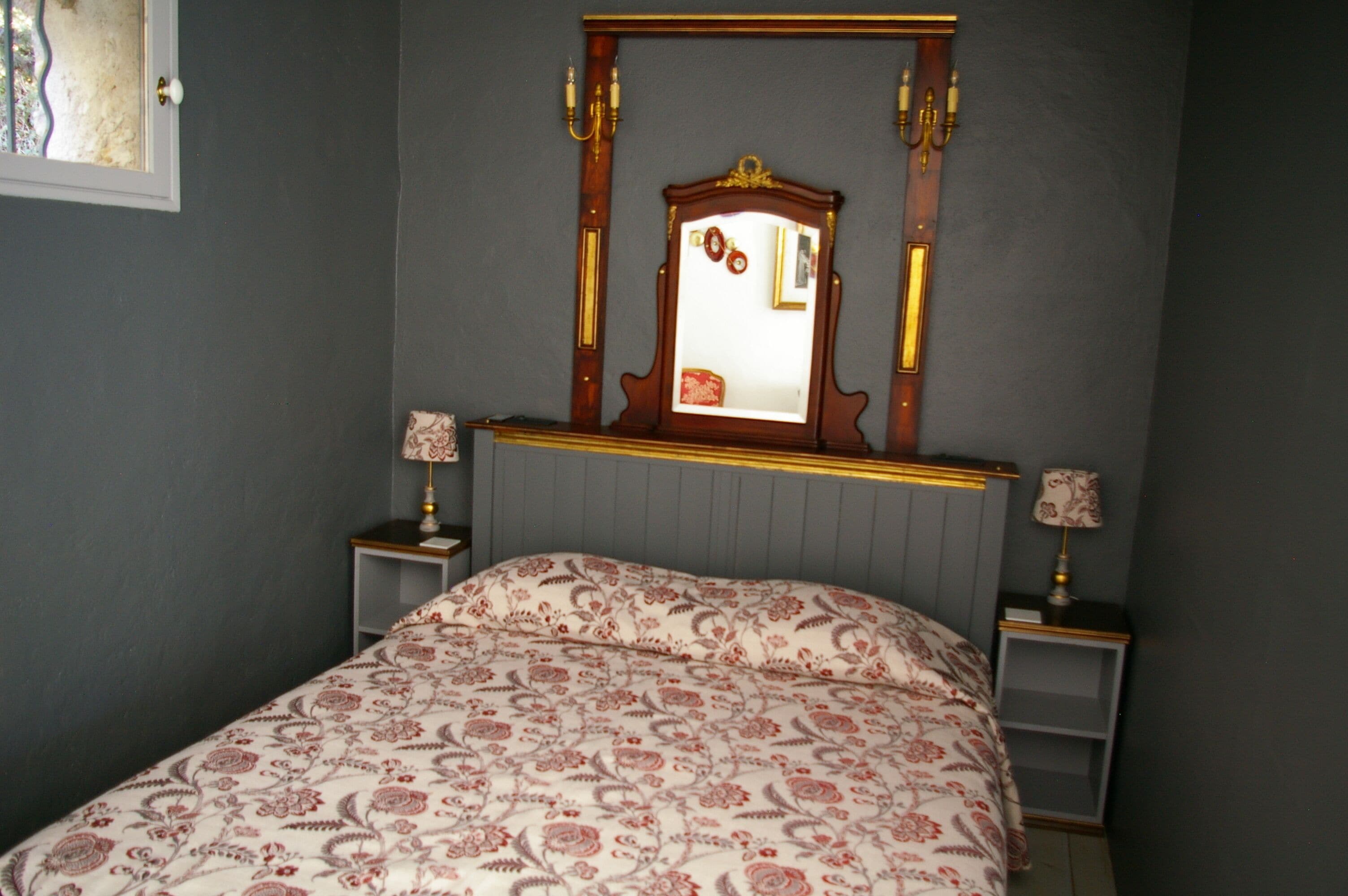 A bedroom with a bed, two bedside tables, a mirror, and a window.