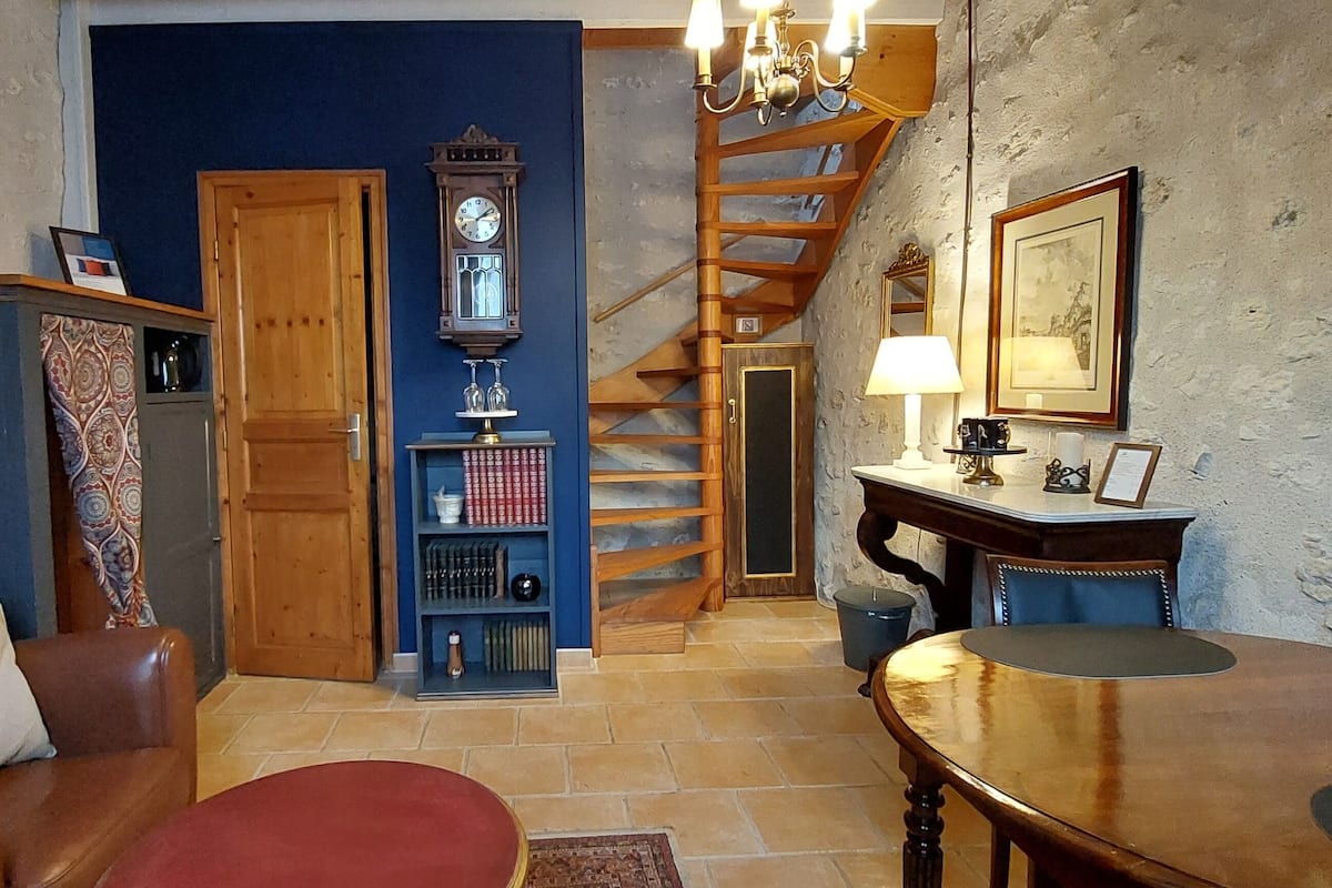 A living room with a brown leather sofa, a red armchair, a wooden coffee table, a blue wall, a wooden staircase, a clock, a bookshelf, and a framed picture on the wall.