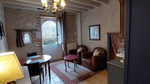 A room with a dining table, two chairs, a lamp, a window with curtains, and a chandelier. - La Source de Bury (Valencisse)