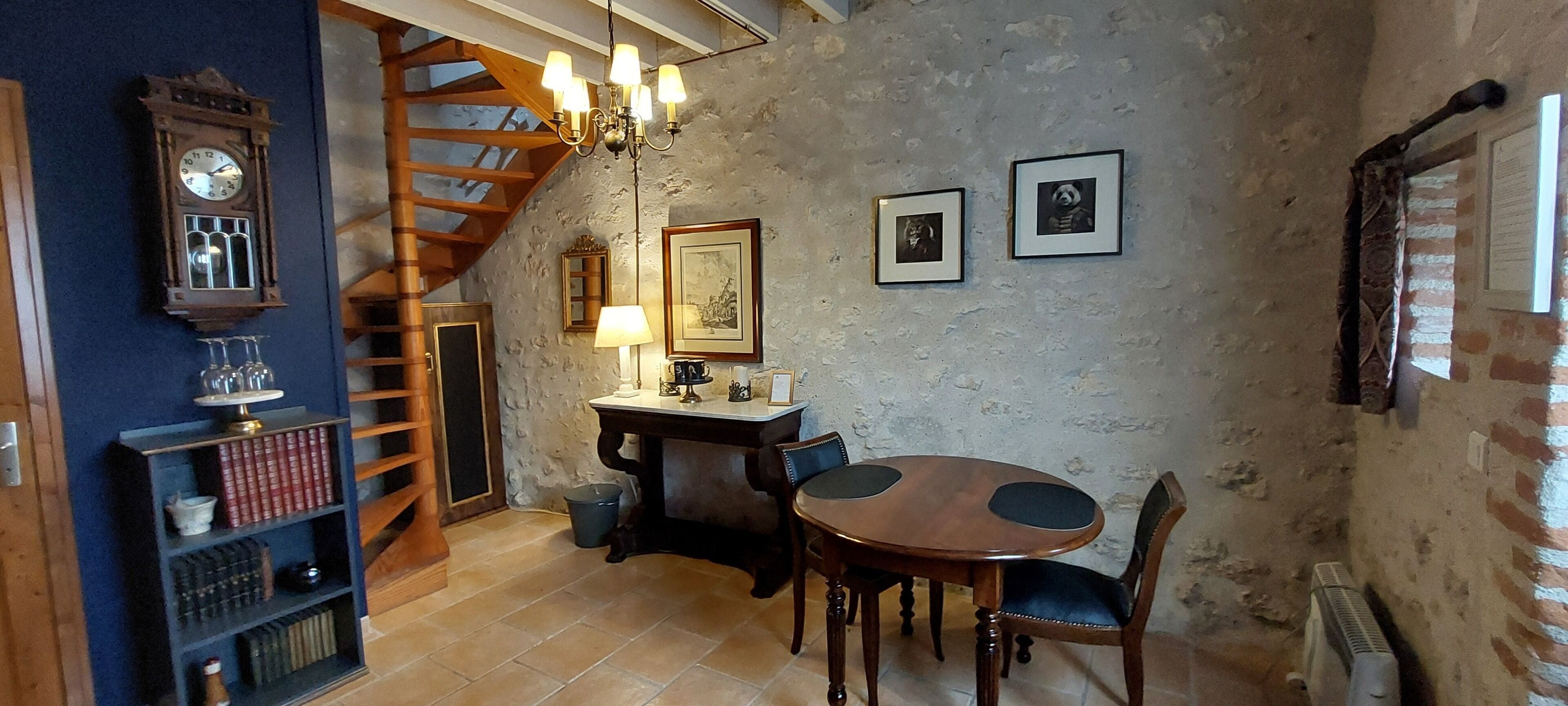 A dining area with a wooden table and chairs, a chandelier, a clock, and framed pictures on the wall.