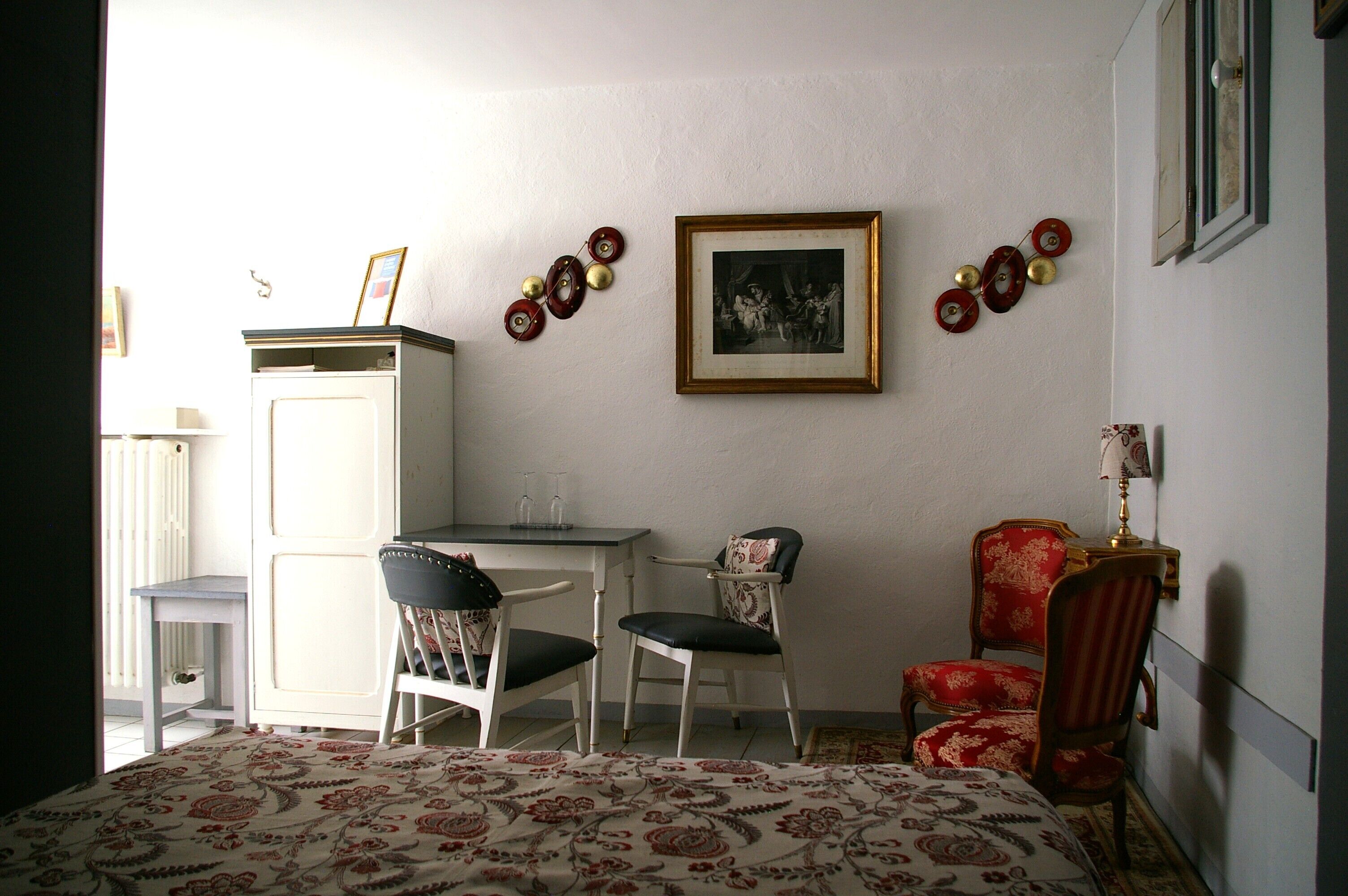 A room with a bed, two chairs, a small table, a cabinet, and a wall-mounted picture.