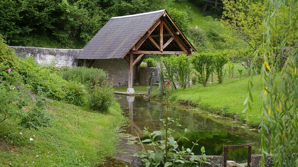 A rustic wooden structure with a sloped roof, situated beside a calm waterway. - La Source de Bury (Valencisse)