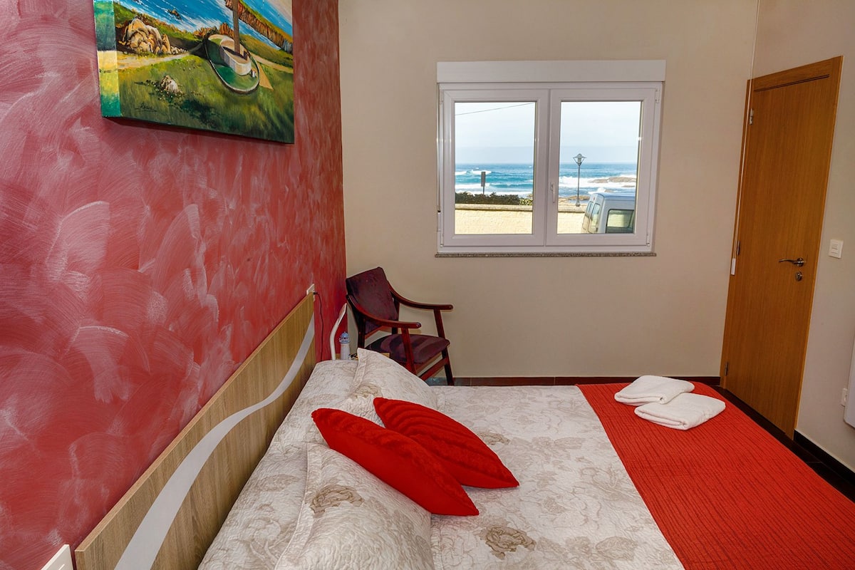 Habitación de hotel con cama, una silla, ventana y vista al mar, además de un cuadro en la pared.