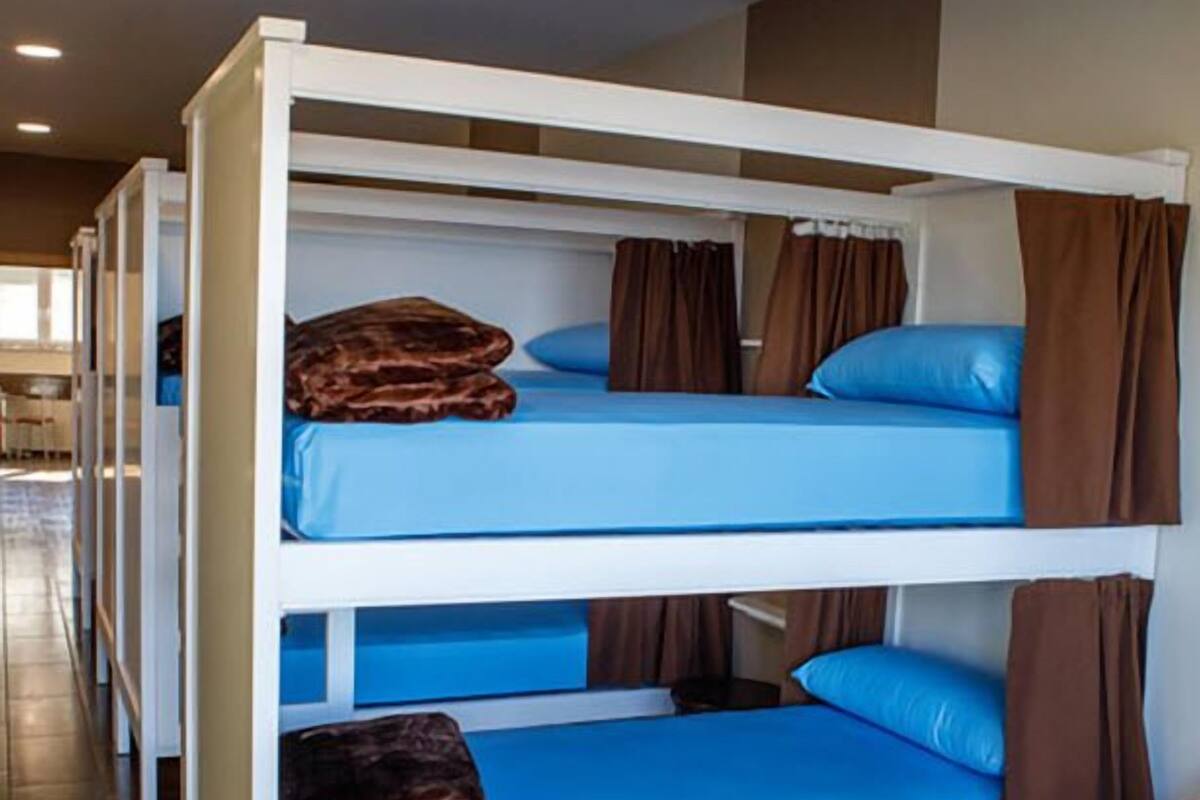 Unas literas en fila con ropa de cama azul y cortinas marrones.