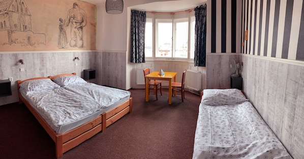 Une chambre avec deux lits, une table en bois, une chaise et une fenêtre avec des rideaux.