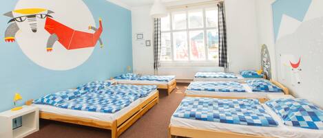 A children's room with four beds, each with blue and white checkered bedding. There is a large wall mural of a cartoon character.